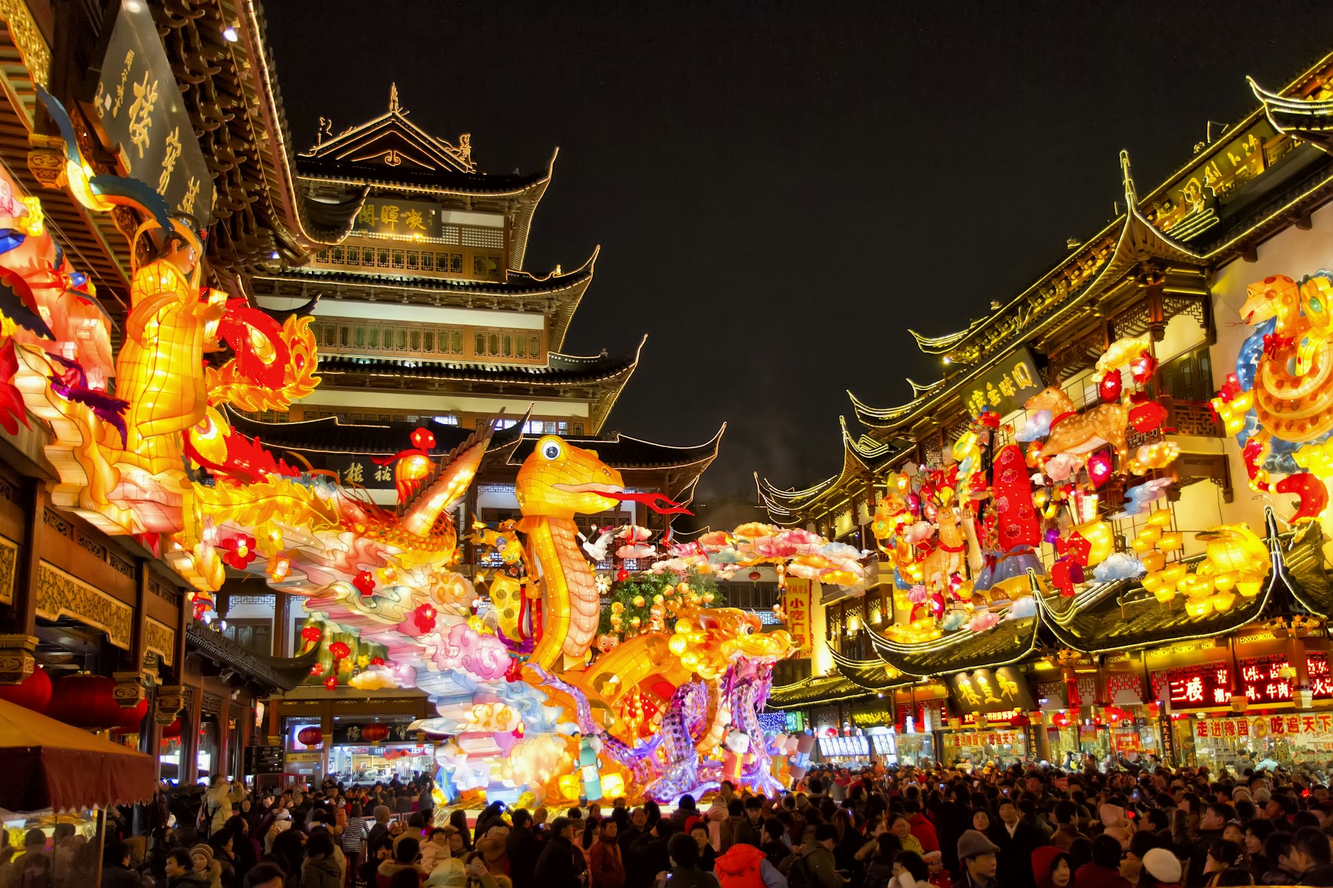 Huge illuminated lanterns of snakes in front of pagodas at night, with crowds of people underneath